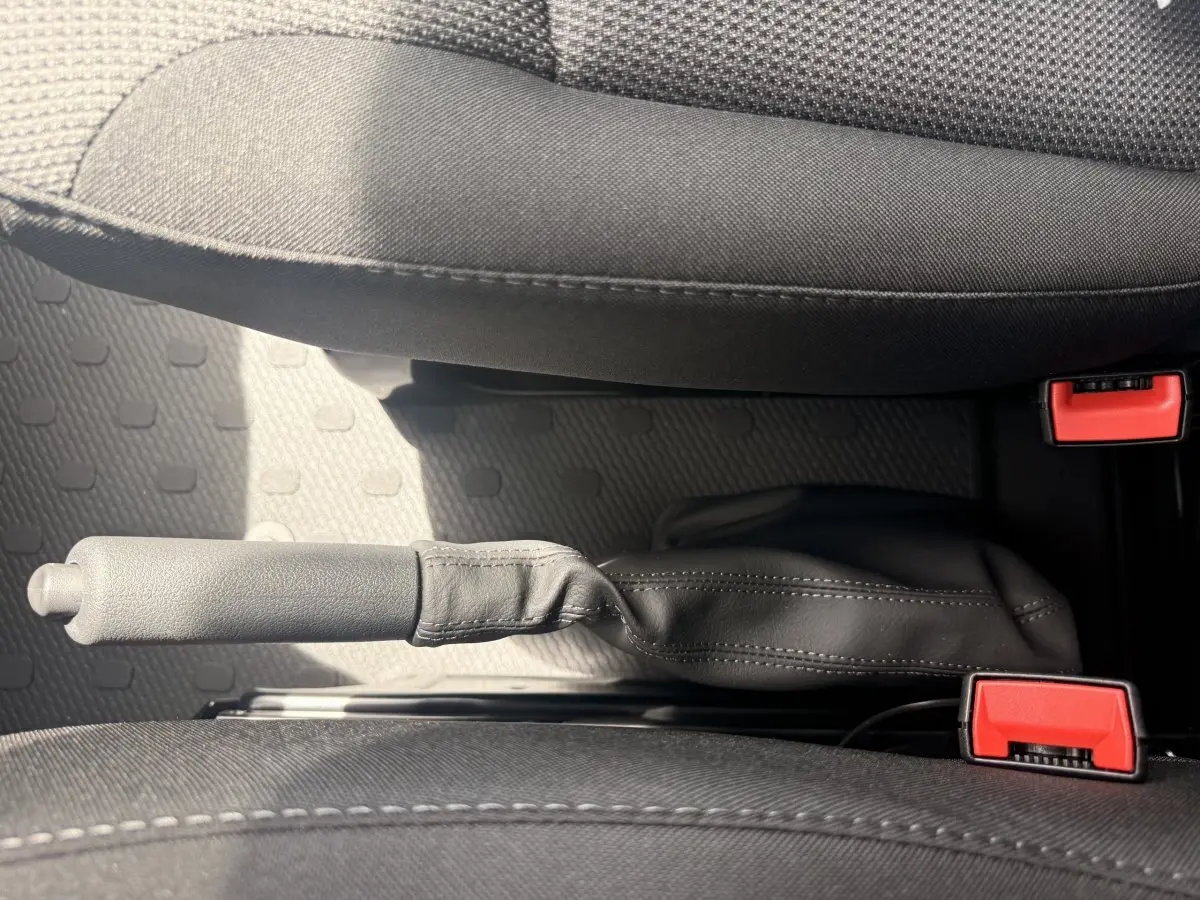 Vue rapprochée de la poignée de frein à main en cuir noir entre les sièges avant gris foncé du Renault Trafic Fourgon blanc.