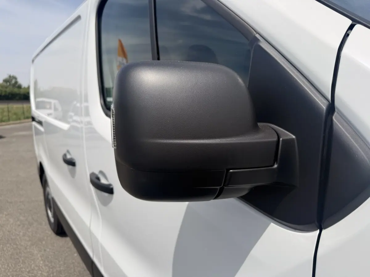 Rétroviseur noir en gros plan sur le côté gauche d’un Renault Trafic Fourgon blanc, vue avant latérale.