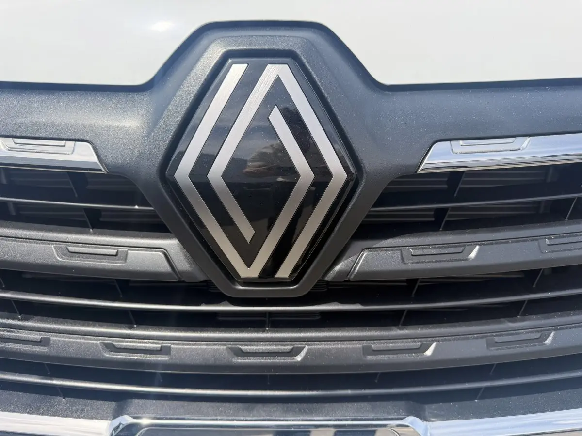 Gros plan sur la calandre noire avec le logo Renault argenté du Trafic Fourgon blanc, vue frontale rapprochée.