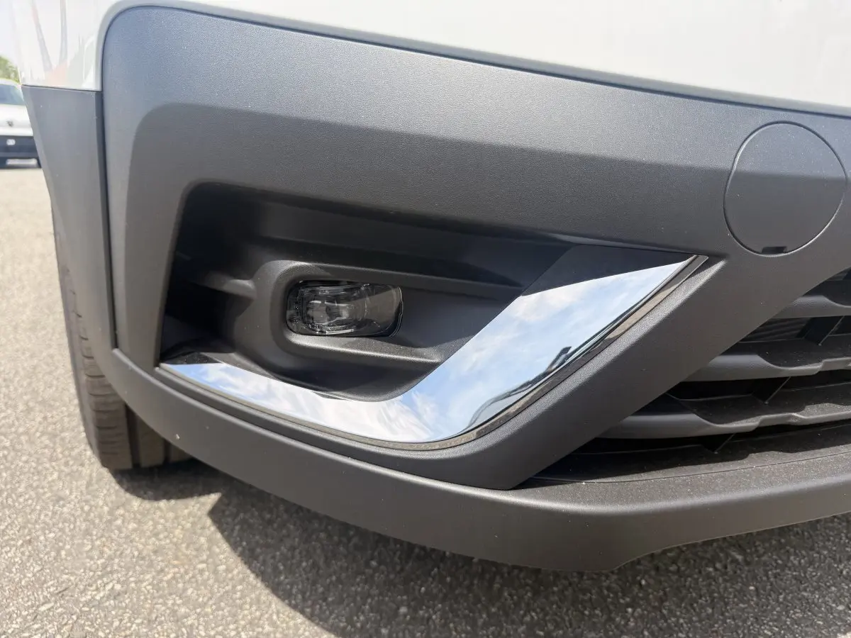 Gros plan sur le pare-chocs avant droit blanc du Renault Trafic Fourgon avec antibrouillard et insert chromé.