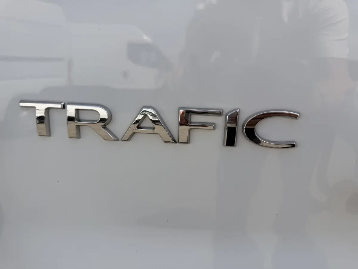 Gros plan sur l’inscription chromée TRAFIC sur la porte arrière d’un fourgon Renault Trafic blanc.