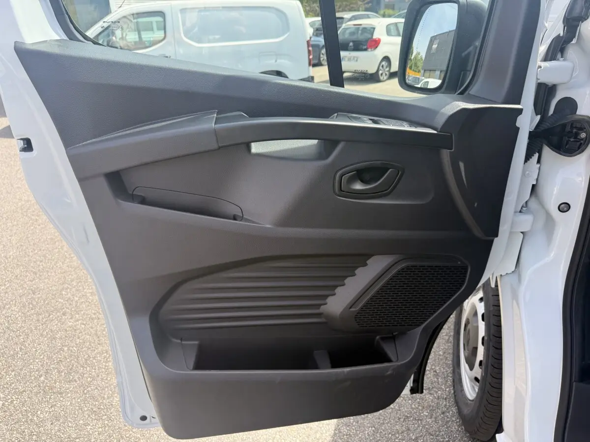Vue de profil de la porte avant gauche ouverte du Renault Trafic Fourgon blanc, avec panneau intérieur noir et haut-parleur intégré.