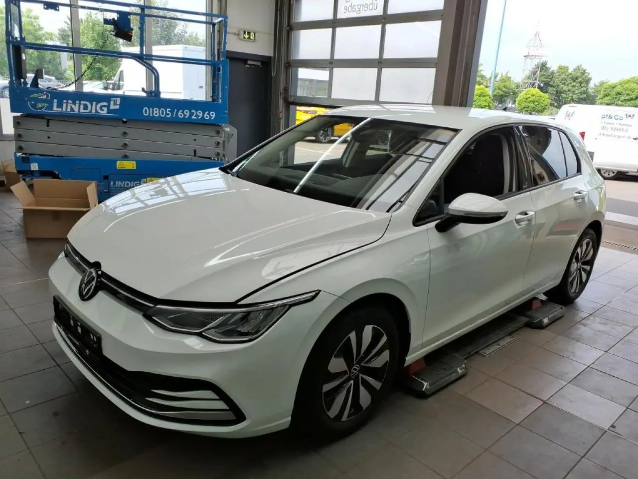 Volkswagen Golf 8 blanche vue 3/4 avant droit en intérieur avec jantes distinctives et phares LED.