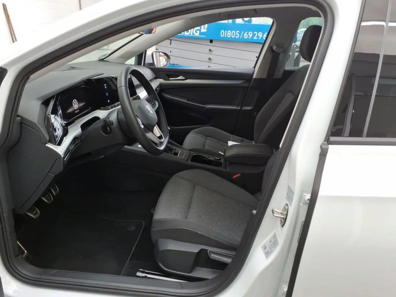 Intérieur de la Volkswagen Golf 8 blanche, vue côté conducteur avec tableau de bord digital et sièges tissu gris.