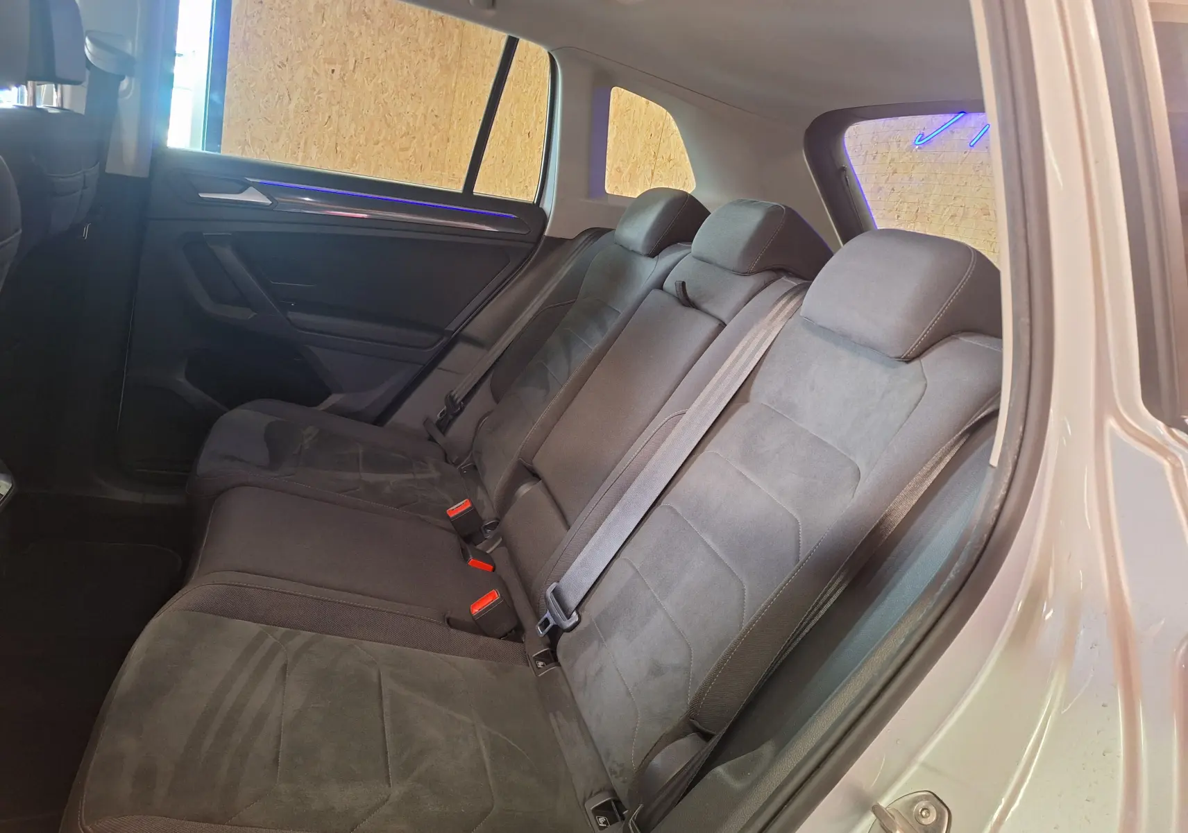 Vue intérieure des sièges arrière en Microfleece gris du Volkswagen Tiguan 2021, avec ceinture de sécurité et éclairage d'ambiance bleu.