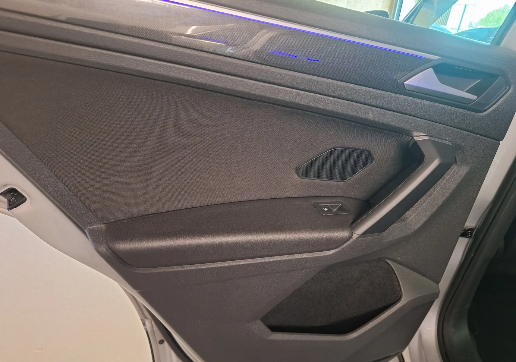 Porte intérieure côté gauche du Volkswagen Tiguan gris 2021, avec éclairage d'ambiance bleu et commande de vitre électrique.
