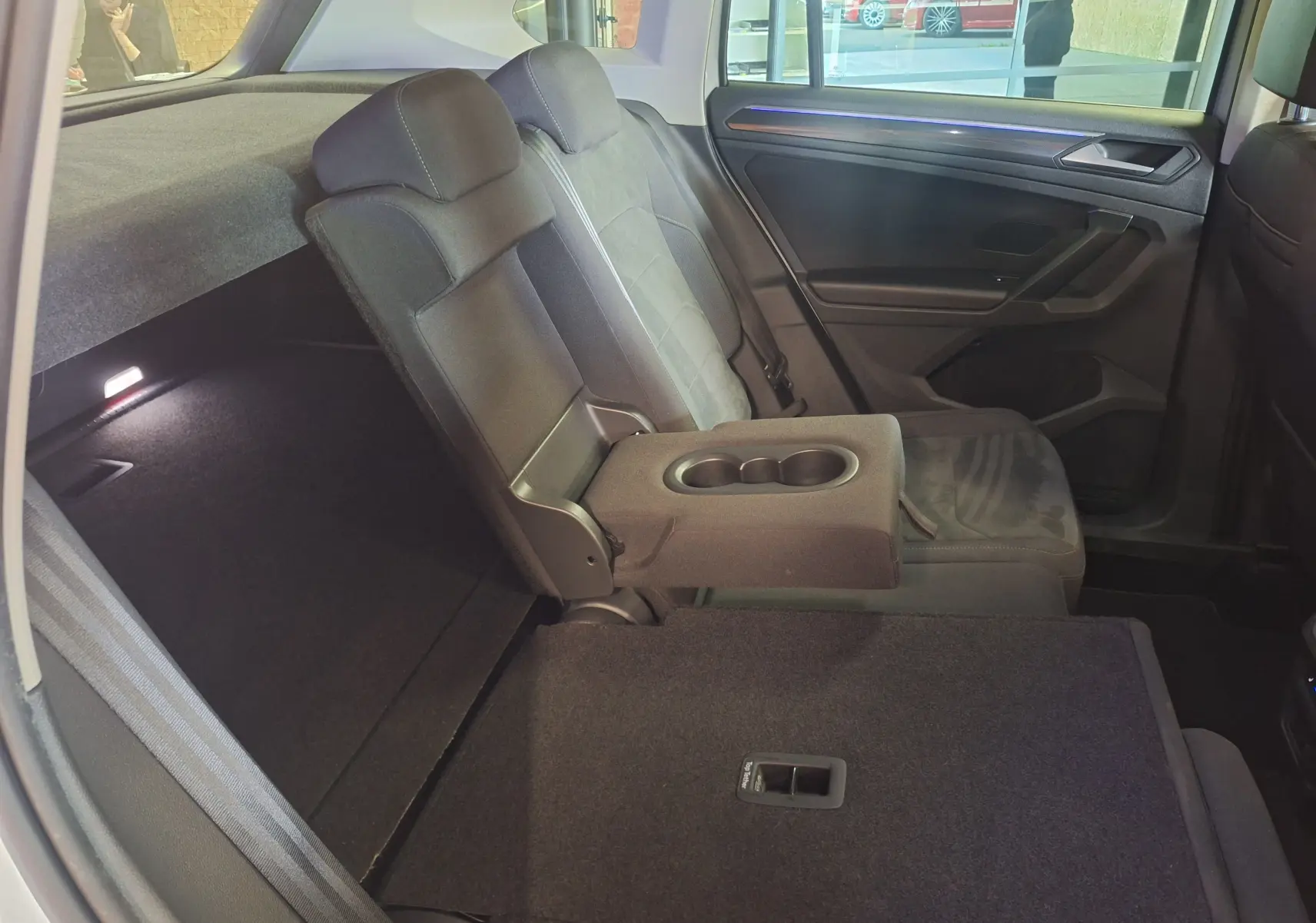 Vue intérieure arrière droite du Volkswagen Tiguan gris, avec accoudoir central relevé et siège rabattable.