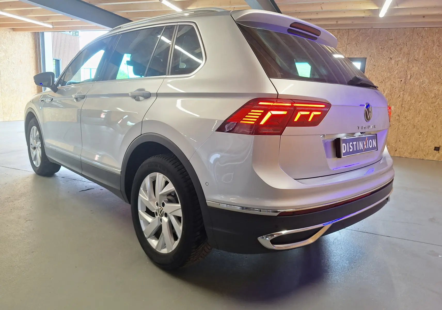 Vue 3/4 arrière droite d'un Volkswagen Tiguan gris métallisé avec feux arrière LED allumés et jantes alliage 18 pouces.