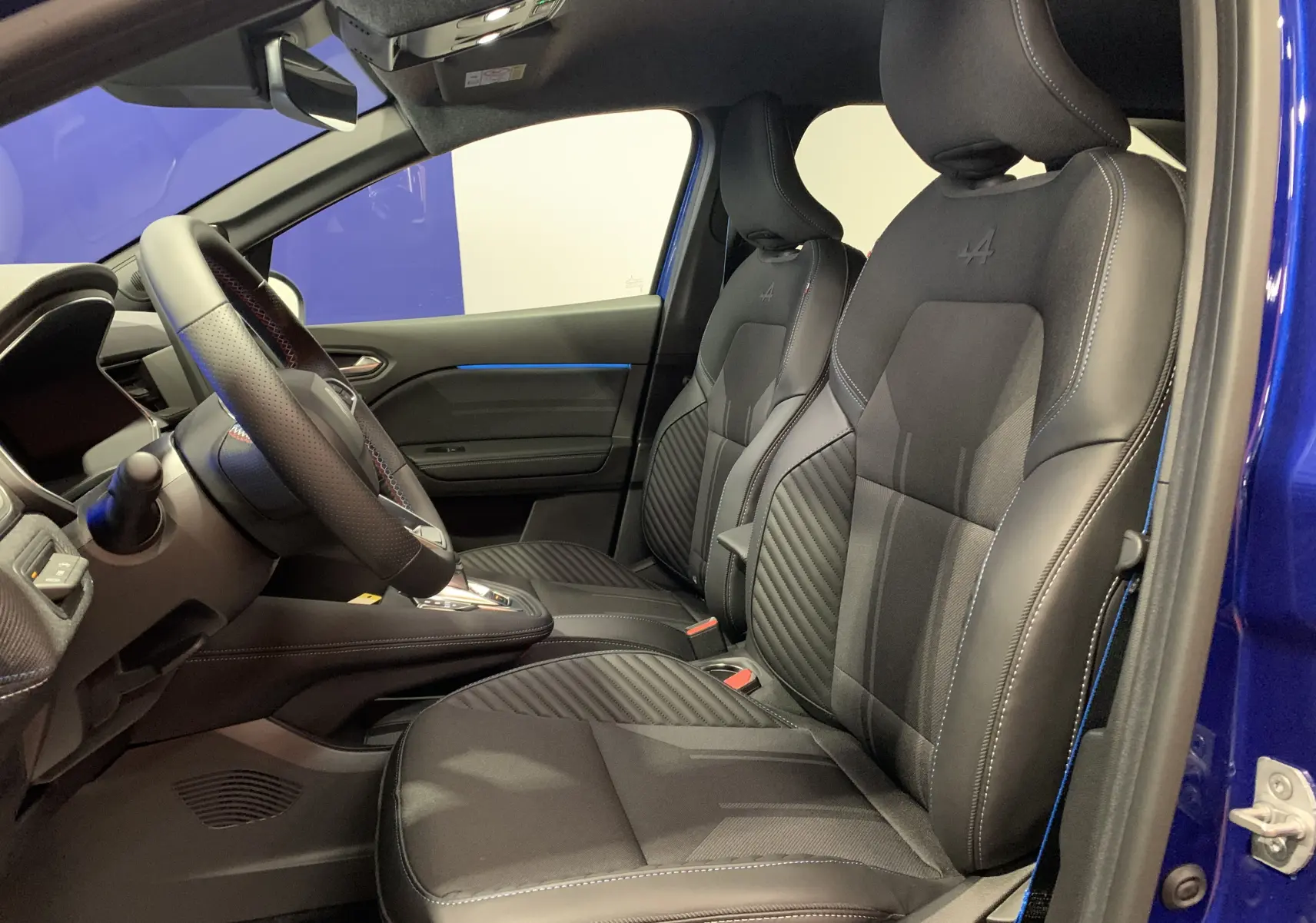 Vue intérieure côté conducteur de la Renault Symbioz E-Tech hybride 2025 avec sièges noirs et surpiqûres bleues, portière bleu iron ouverte.