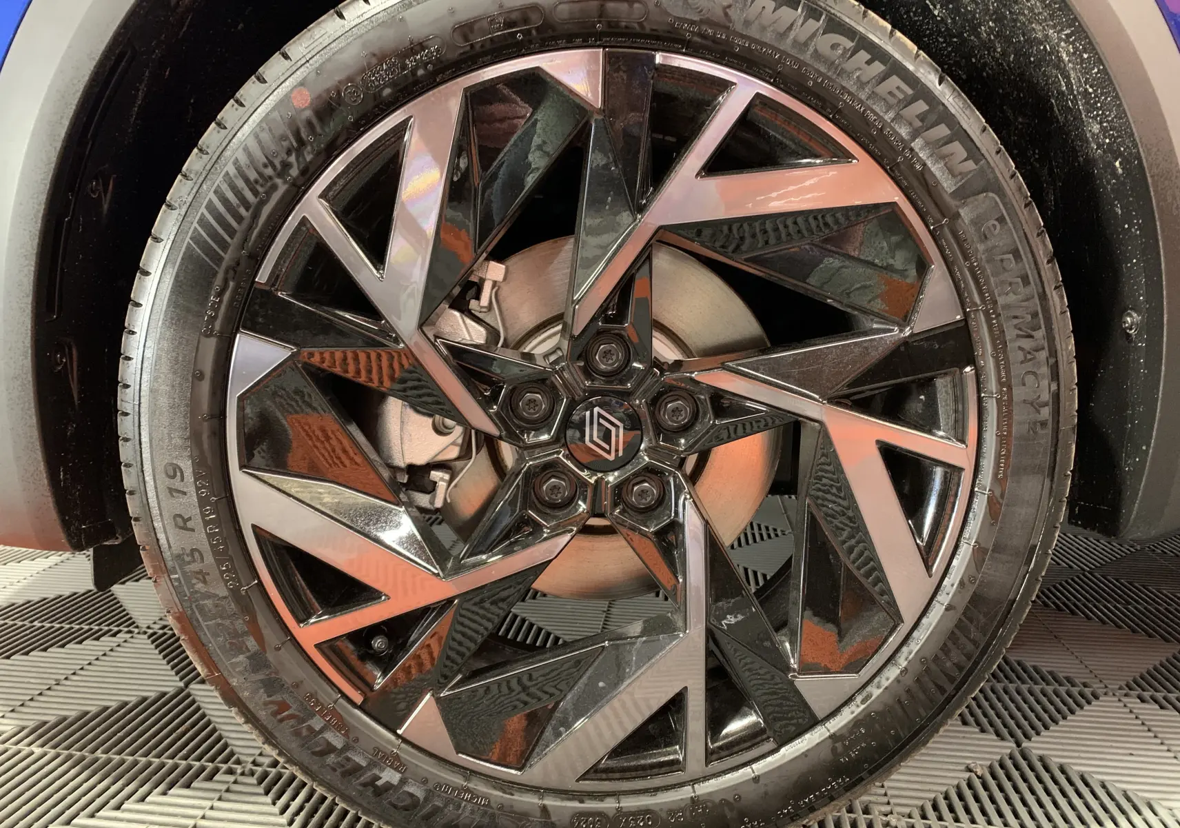 Gros plan sur la jante noire et argentée au design géométrique du Renault Symbioz Bleu Iron, pneu Michelin visible.