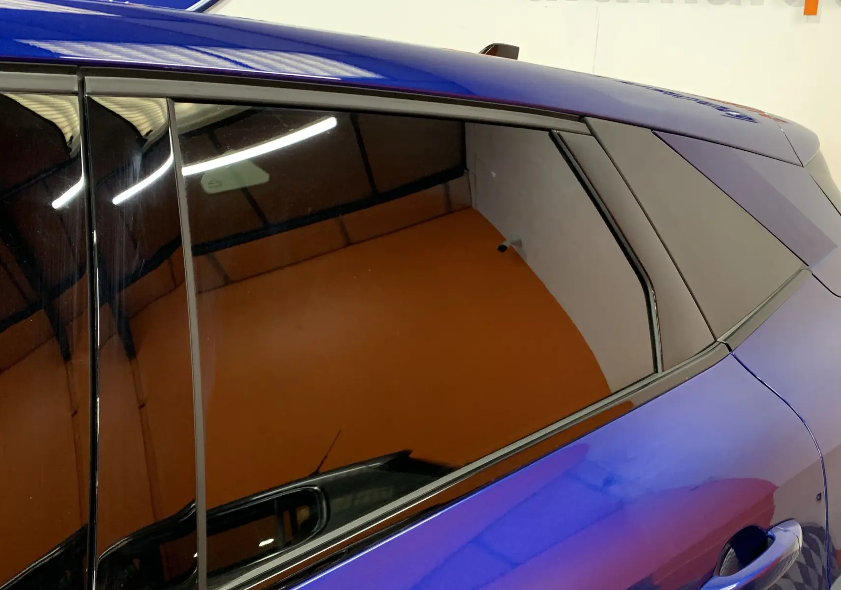 Gros plan sur la vitre arrière côté droit d'une Renault Symbioz bleu iron avec reflet intérieur orangé.