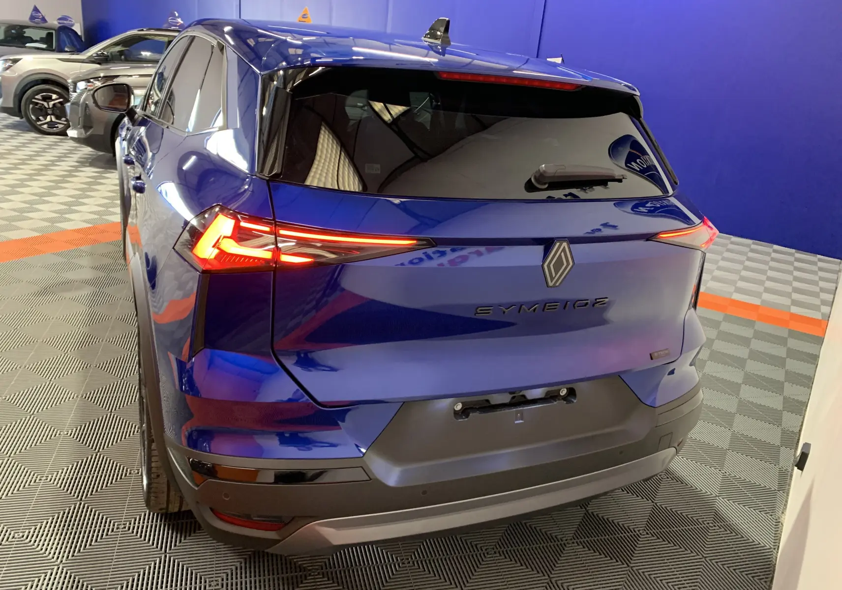 Vue 3/4 arrière du Renault SYMBIOZ bleu iron avec feux LED allumés et hayon motorisé mains libres visible.