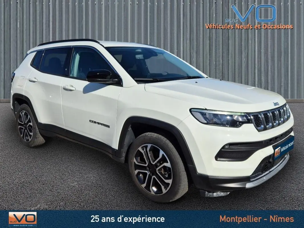 Jeep Compass blanc vue 3/4 avant droit avec jantes 18 pouces et barres de toit noires sur fond urbain.