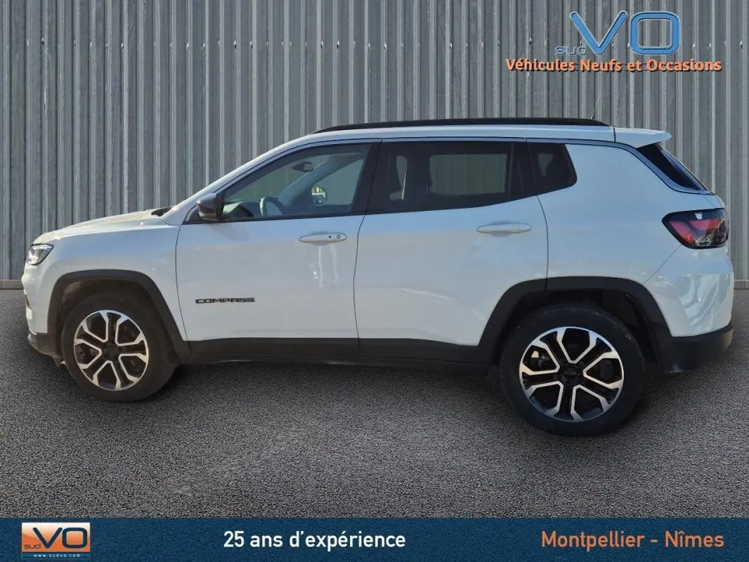 Vue de profil côté gauche d'un Jeep Compass blanc 2023 avec jantes 18 pouces et barres de toit noires.