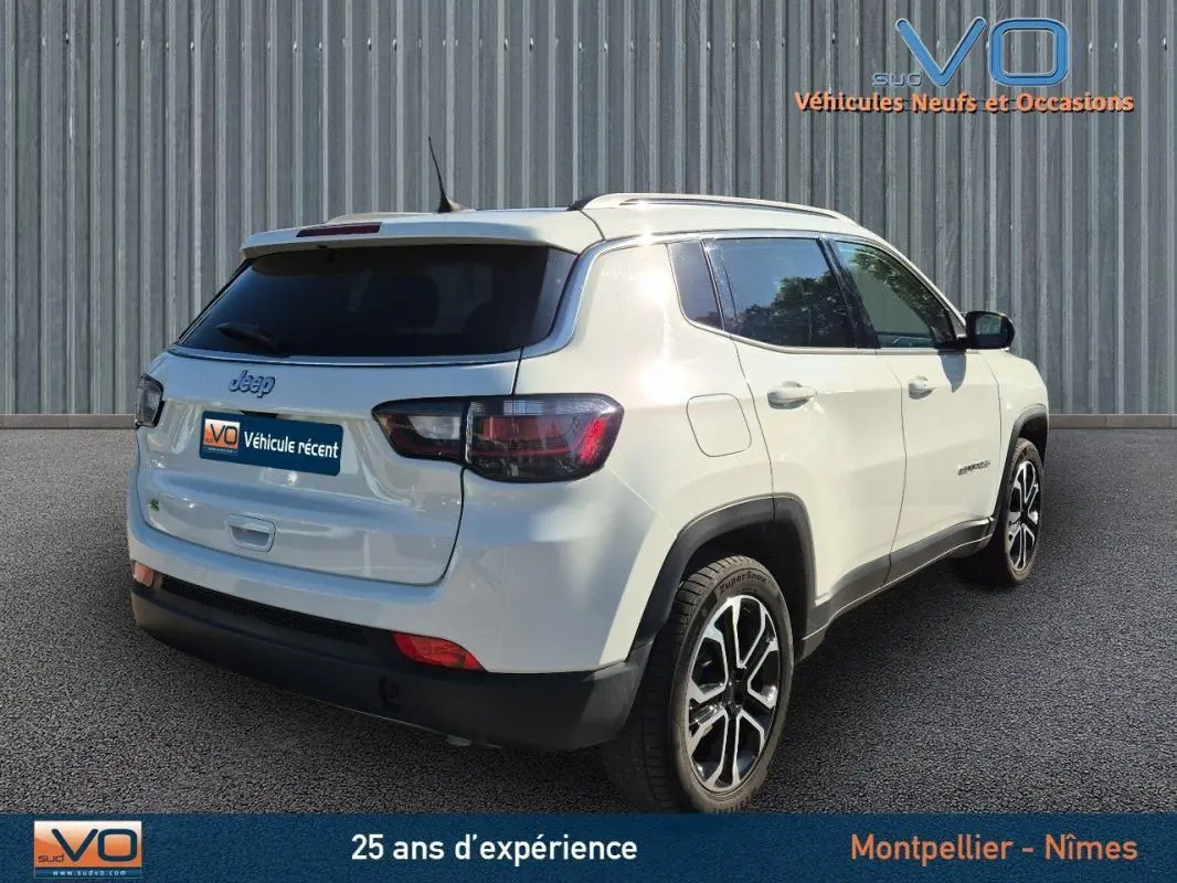 Vue 3/4 arrière droite d'un Jeep Compass blanc 2023 avec barres de toit et jantes 18 pouces visibles.