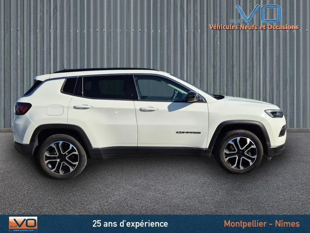 Profil côté gauche d'un Jeep Compass blanc 2023 avec jantes 18 pouces et barres de toit visibles.