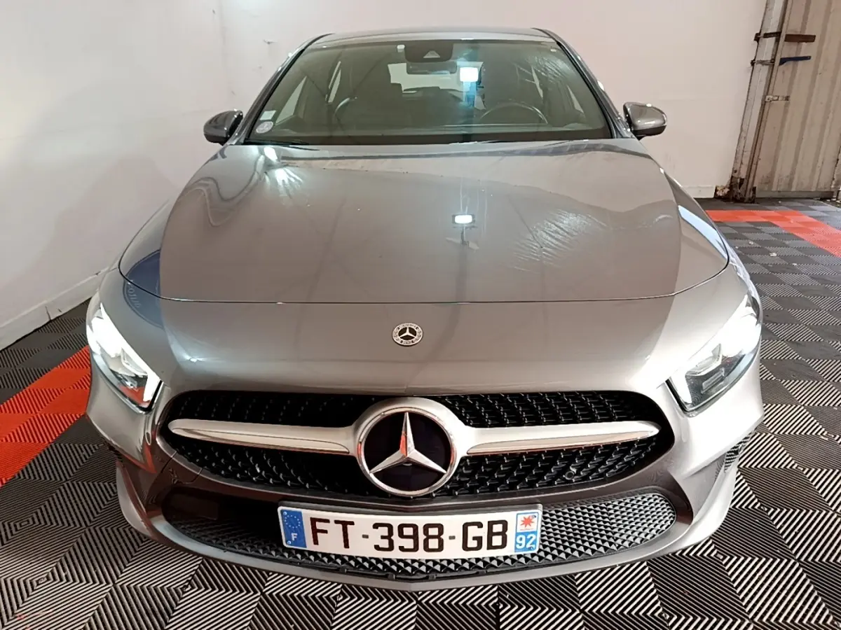 Vue avant d'une Mercedes Classe A gris foncé avec calandre étoilée et phares LED allumés dans un garage.
