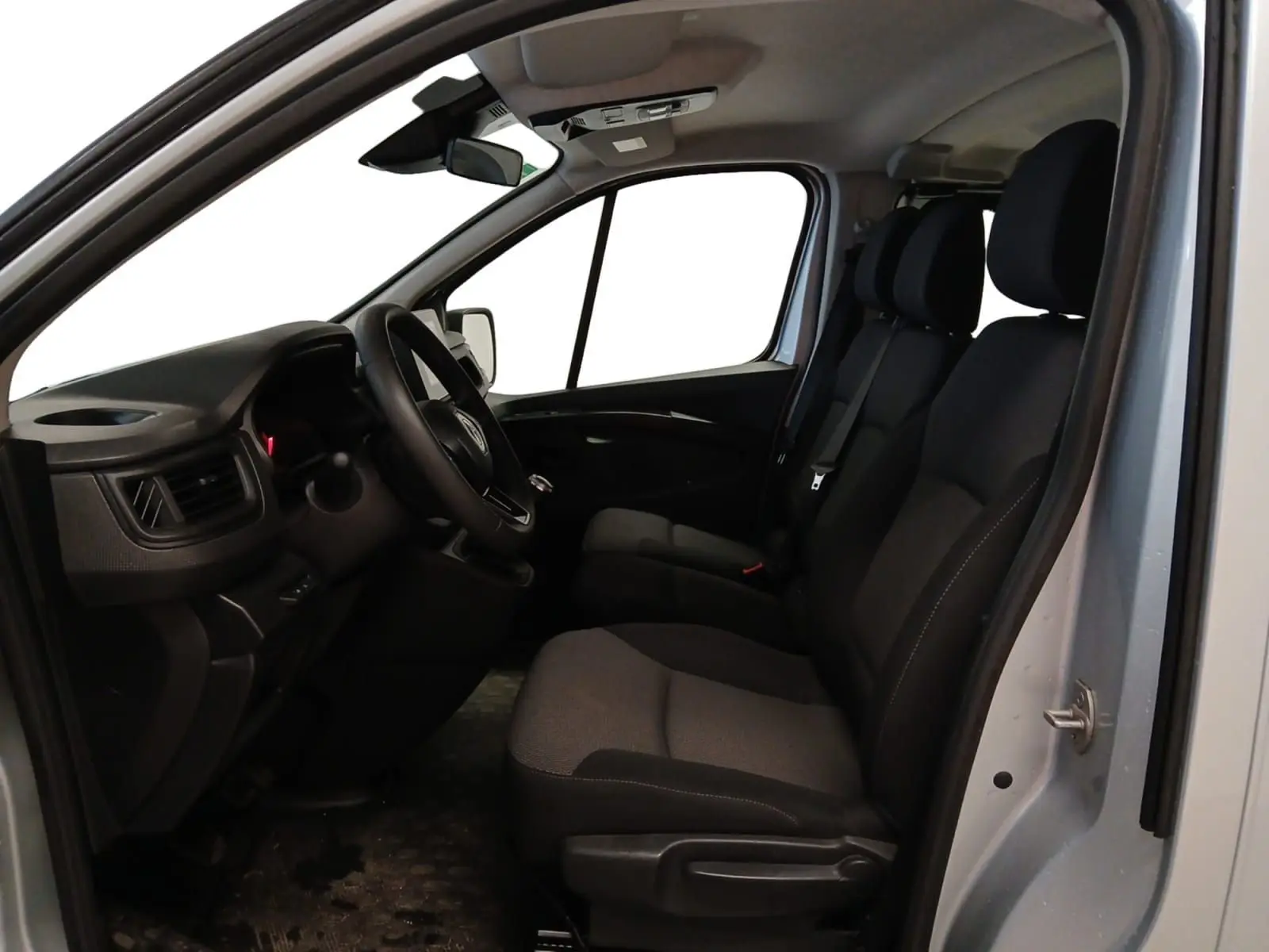 Vue intérieure côté conducteur du Renault Trafic Combi gris clair métal 2023, montrant les sièges avant et le tableau de bord.