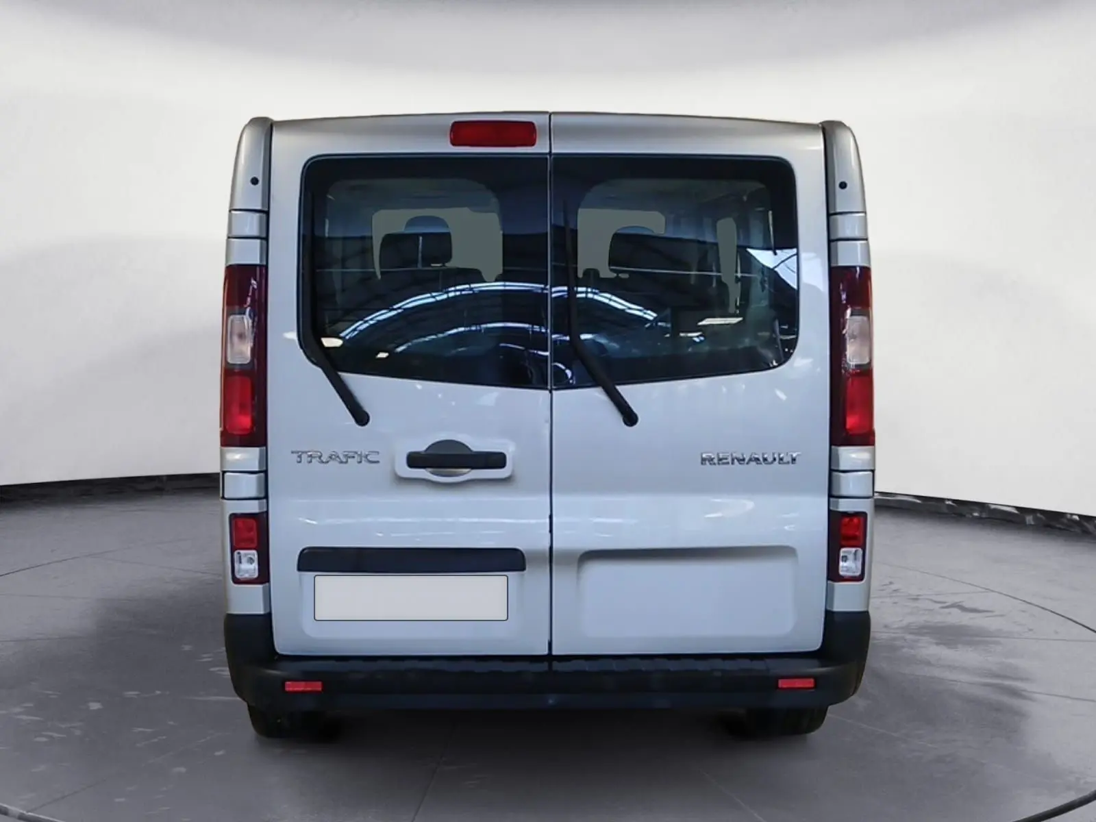 Vue arrière d’un Renault Trafic Combi gris clair métal, portes battantes avec essuie-glaces et feux verticaux rouges.