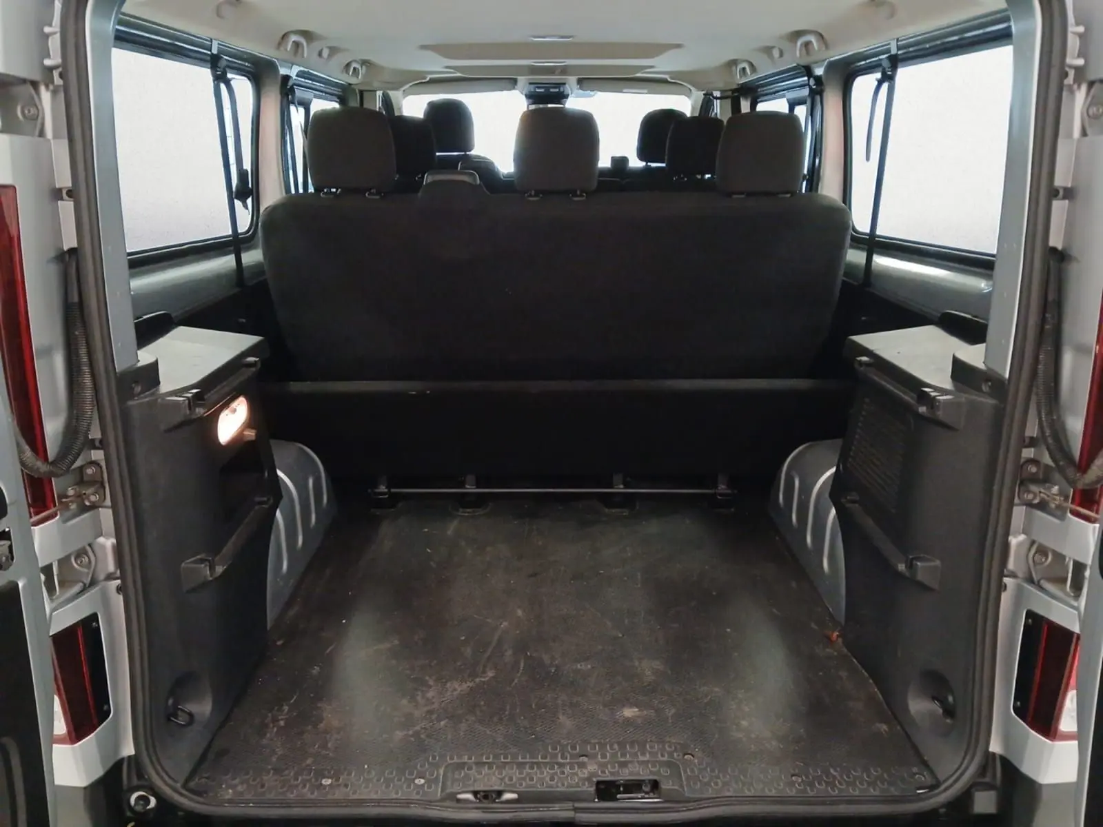 Vue arrière ouverte du Renault Trafic Combi gris clair métal 2023, montrant l'espace de chargement et les sièges passagers noirs.