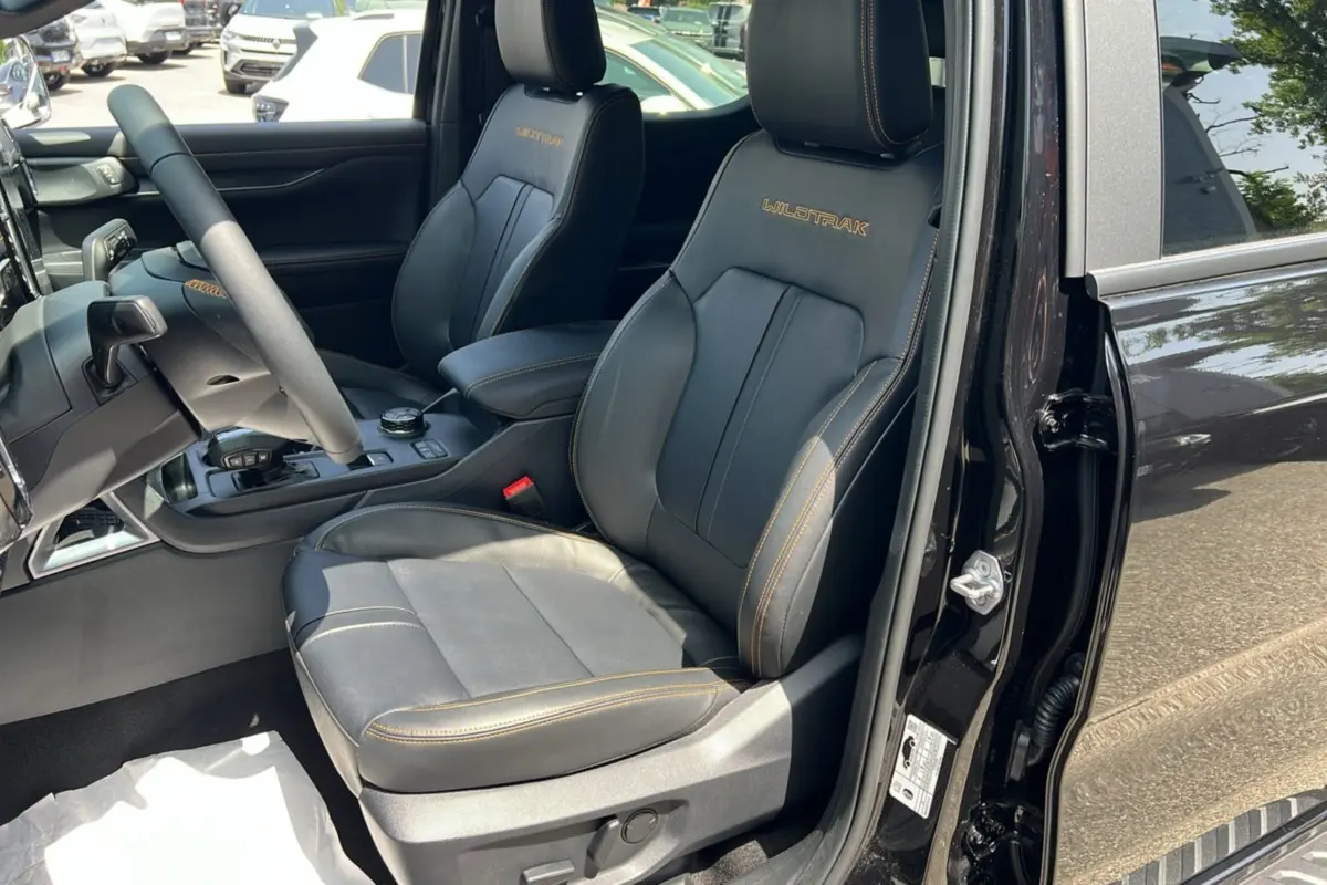 Vue intérieure côté conducteur du Ford Ranger Wildtrak Plus 2025 noir agate, sièges cuir avec surpiqûres orange et logo Wildtrak brodé.