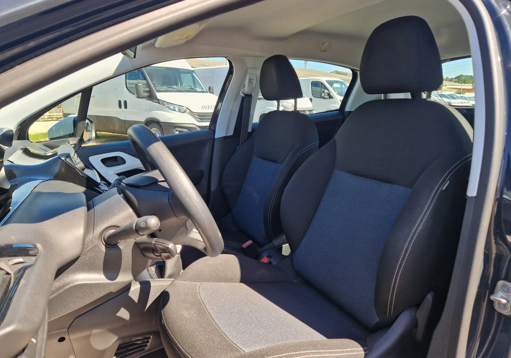 Vue intérieure côté conducteur du Peugeot 208 1.2 PureTech 68 Like 2018, sièges tissu noir et bleu, volant et tableau de bord visibles.