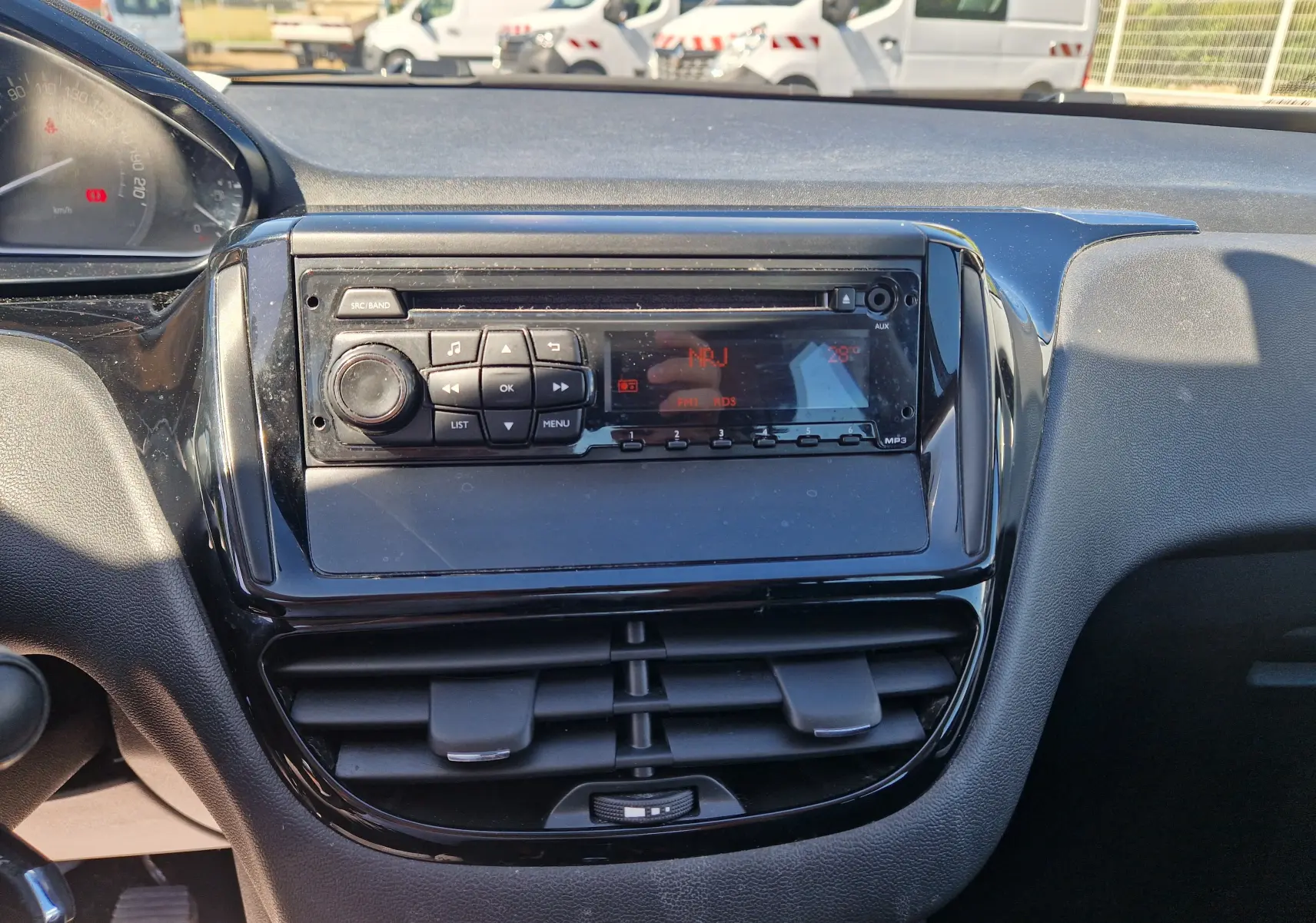 Vue rapprochée du tableau de bord de la Peugeot 208 2018 avec autoradio et commandes noires brillantes.