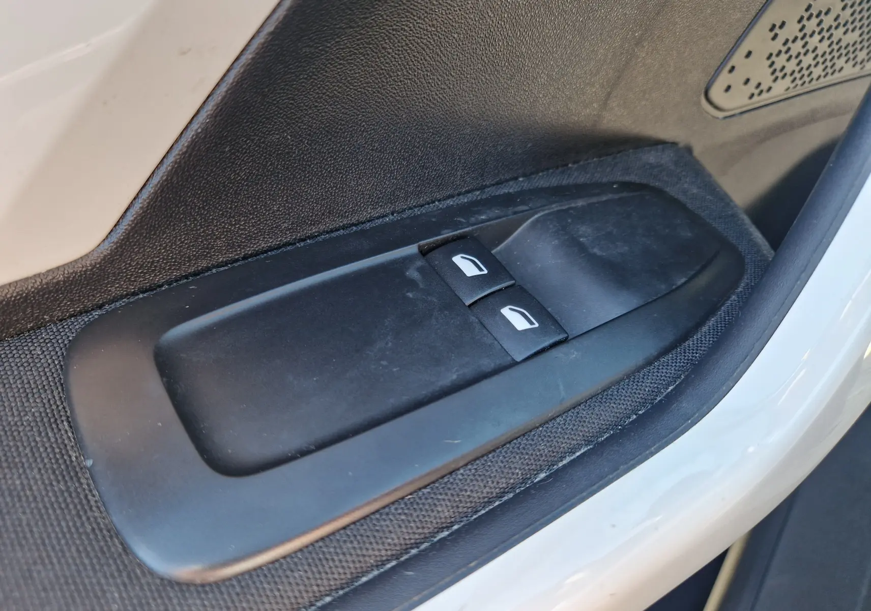 Gros plan sur les commandes des vitres électriques côté conducteur d’une Peugeot 208 gris Hurricane, intérieur noir.