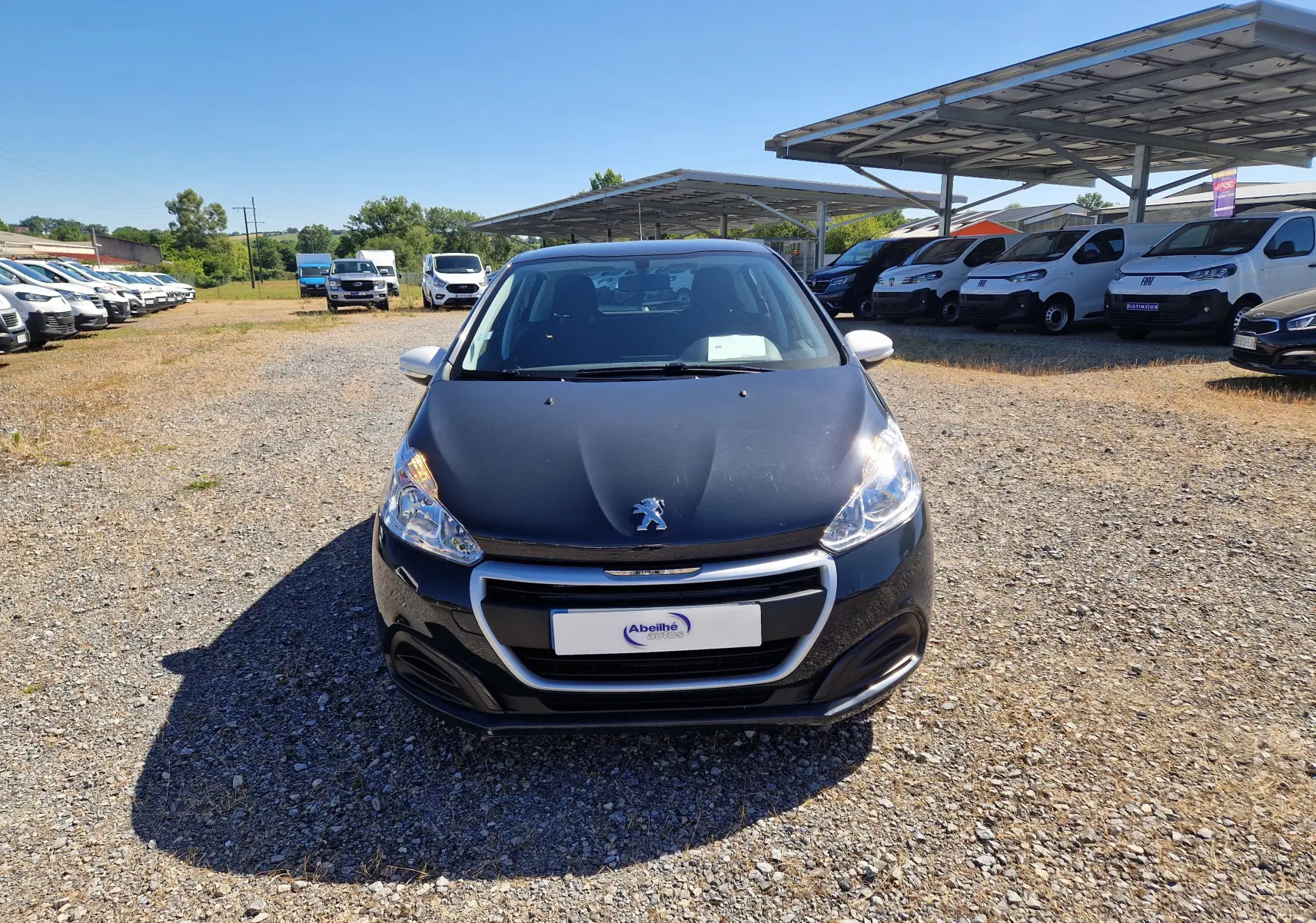 Vue avant d'une Peugeot 208 gris hurricane 2018, avec calandre chromée et phares allumés sur parking extérieur.