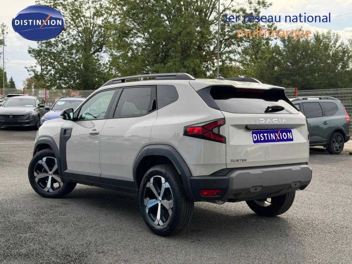 Vue 3/4 arrière droite du Dacia Duster 2025 couleur Sandstone avec jantes alliage et barres de toit noires.