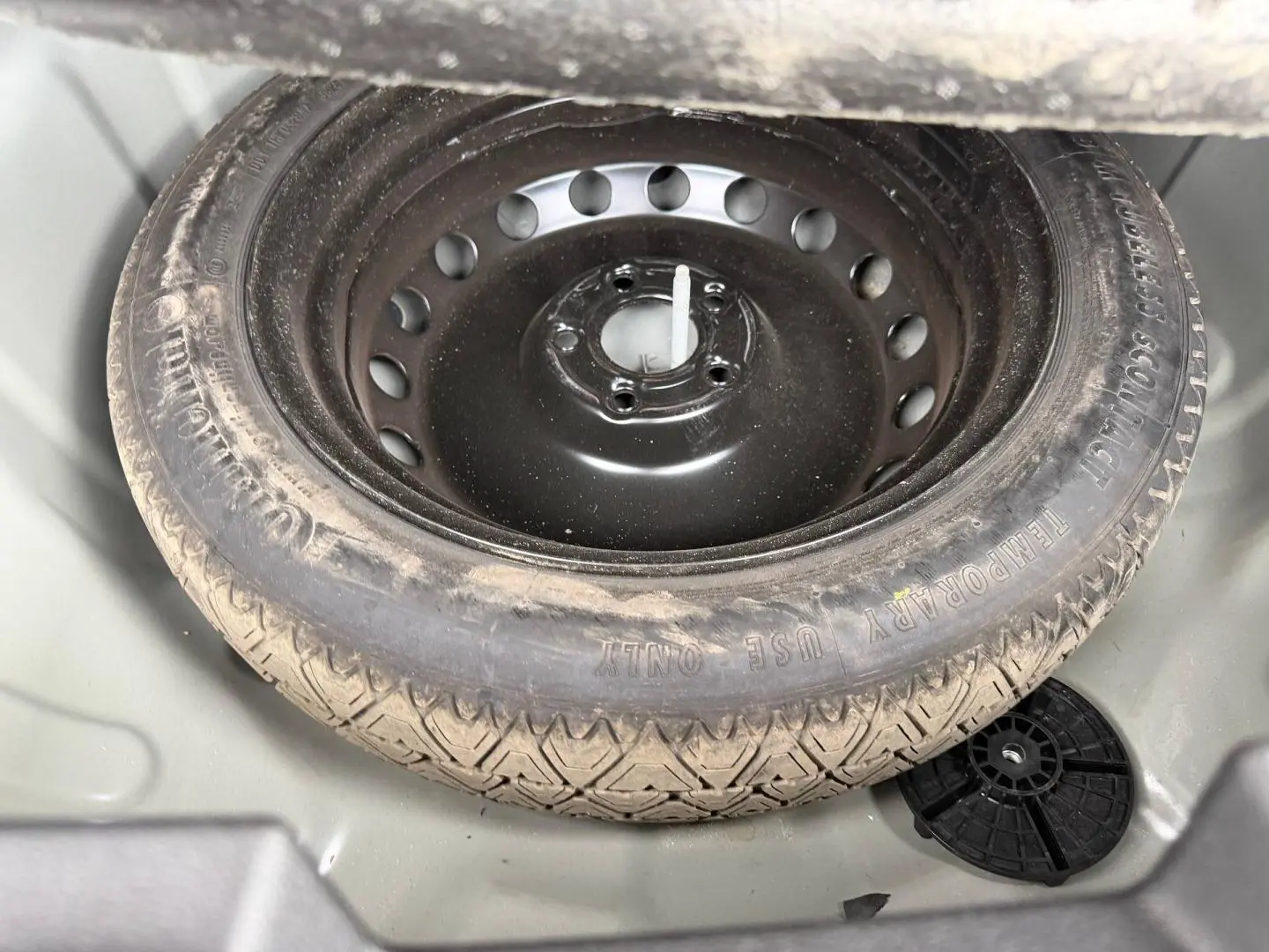 Vue rapprochée de la roue de secours noire dans le coffre gris clair du Dacia Duster 2025 Sandstone.