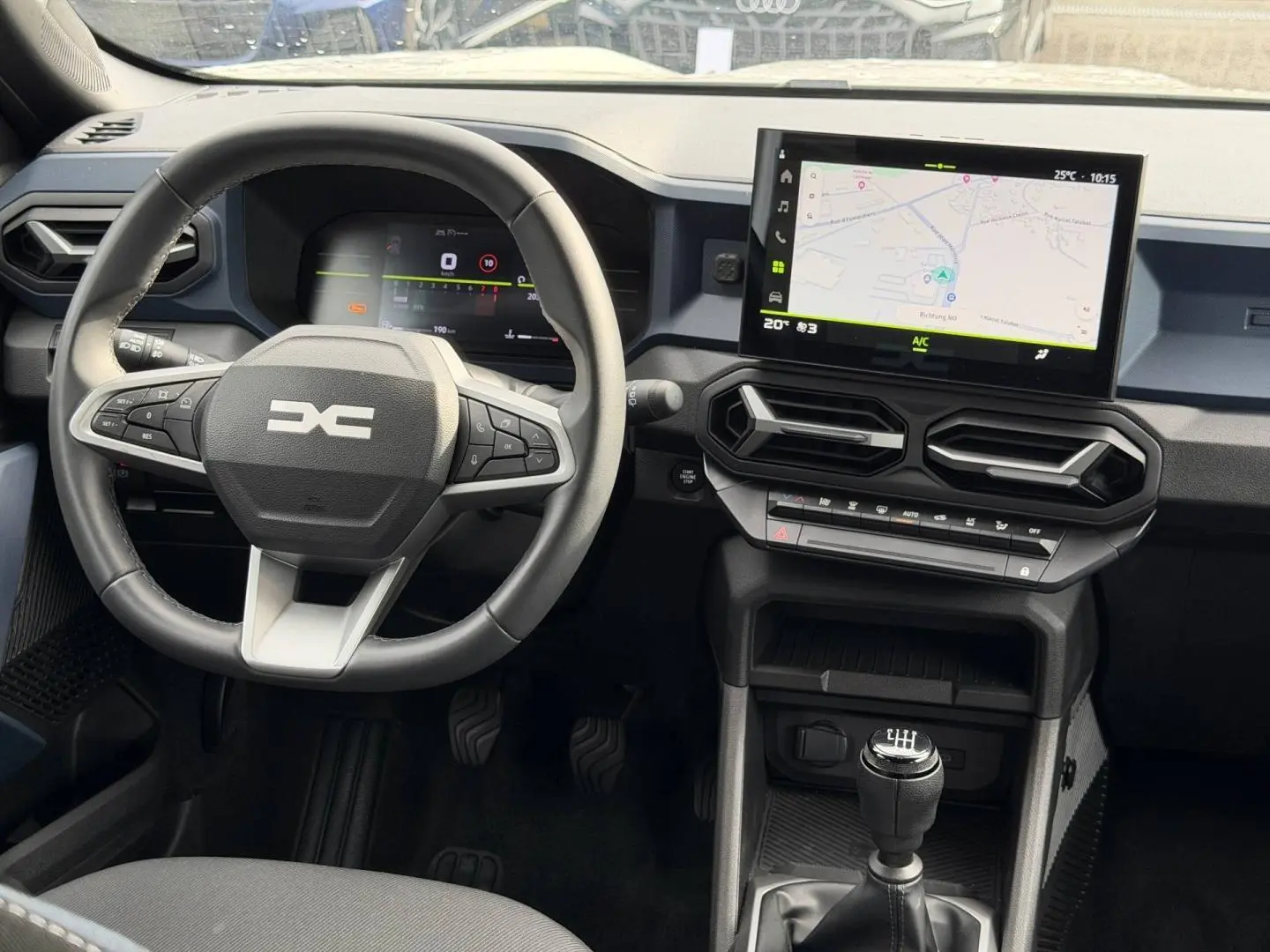 Vue intérieure frontale du tableau de bord du Dacia Duster 2025, avec volant multifonction, écran tactile et levier de vitesse manuel.