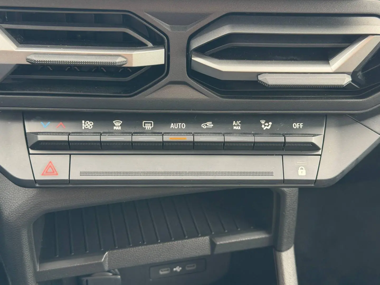 Vue rapprochée de la console centrale du Dacia Duster 2025 sandstone, avec commandes climatisation et prises USB visibles.