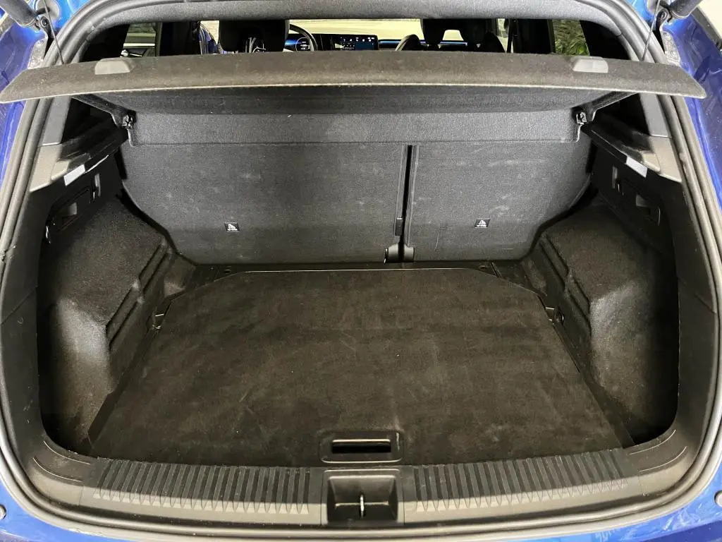 Coffre ouvert vu de l'arrière d'un Renault Austral bleu, avec cache-bagages et intérieur noir.