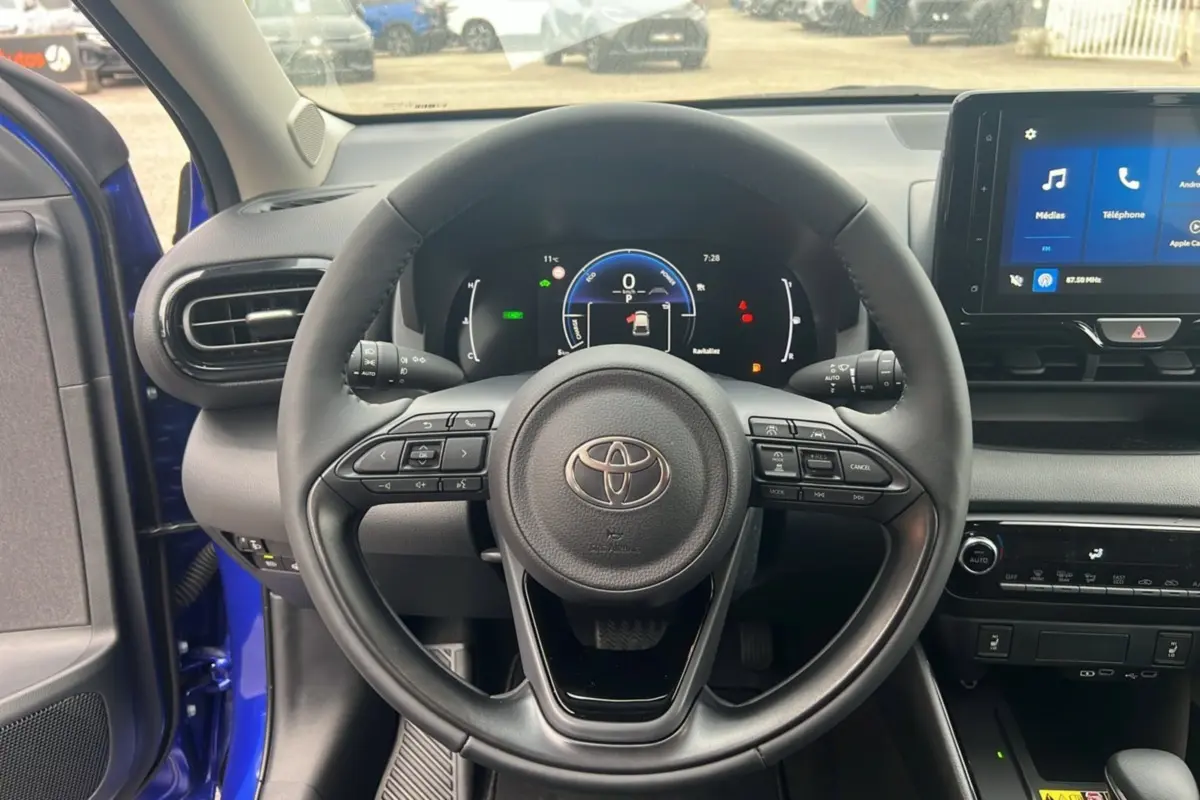 Vue intérieure centrée sur le volant de la Toyota Yaris 2025 bleu genievre avec tableau de bord numérique et écran tactile.