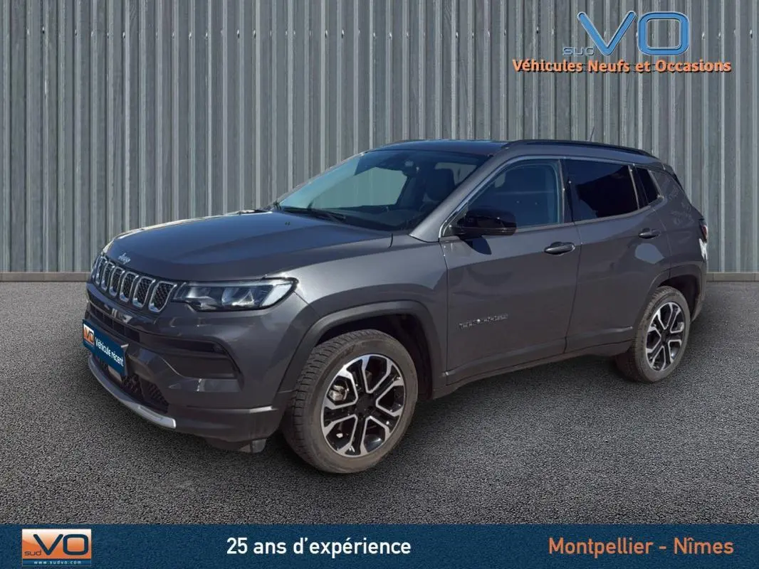 Jeep Compass gris en 3/4 avant droit, avec jantes 18 pouces et barres de toit visibles sur fond urbain.