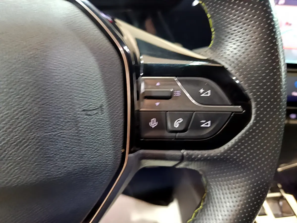Gros plan sur les commandes du volant cuir perforé de la Peugeot 308 PHEV 180 E-EAT8 GT, boutons multifonctions noirs.
