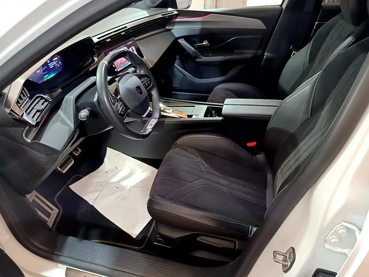 Intérieur côté conducteur du Peugeot 308 PHEV blanc, avec tableau de bord numérique et sièges noirs en tissu et cuir.