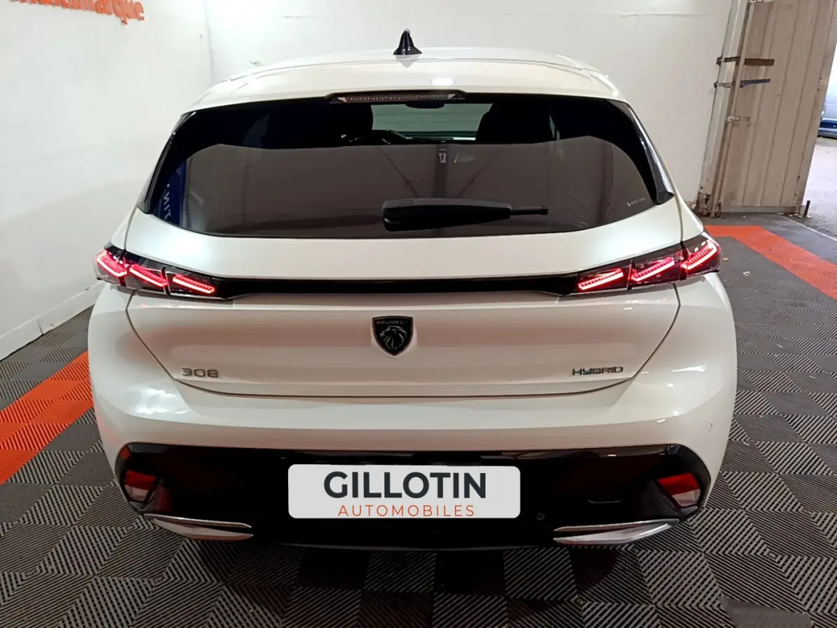 Vue arrière d'une Peugeot 308 PHEV blanche avec feux LED allumés dans un garage showroom.