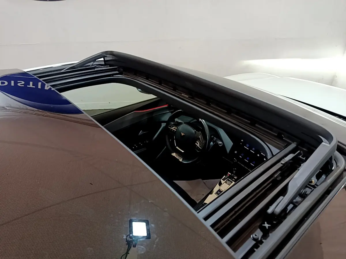 Vue plongeante sur l'intérieur noir d'une Peugeot 308 PHEV 180 E-EAT8 GT blanche avec toit ouvrant panoramique ouvert.