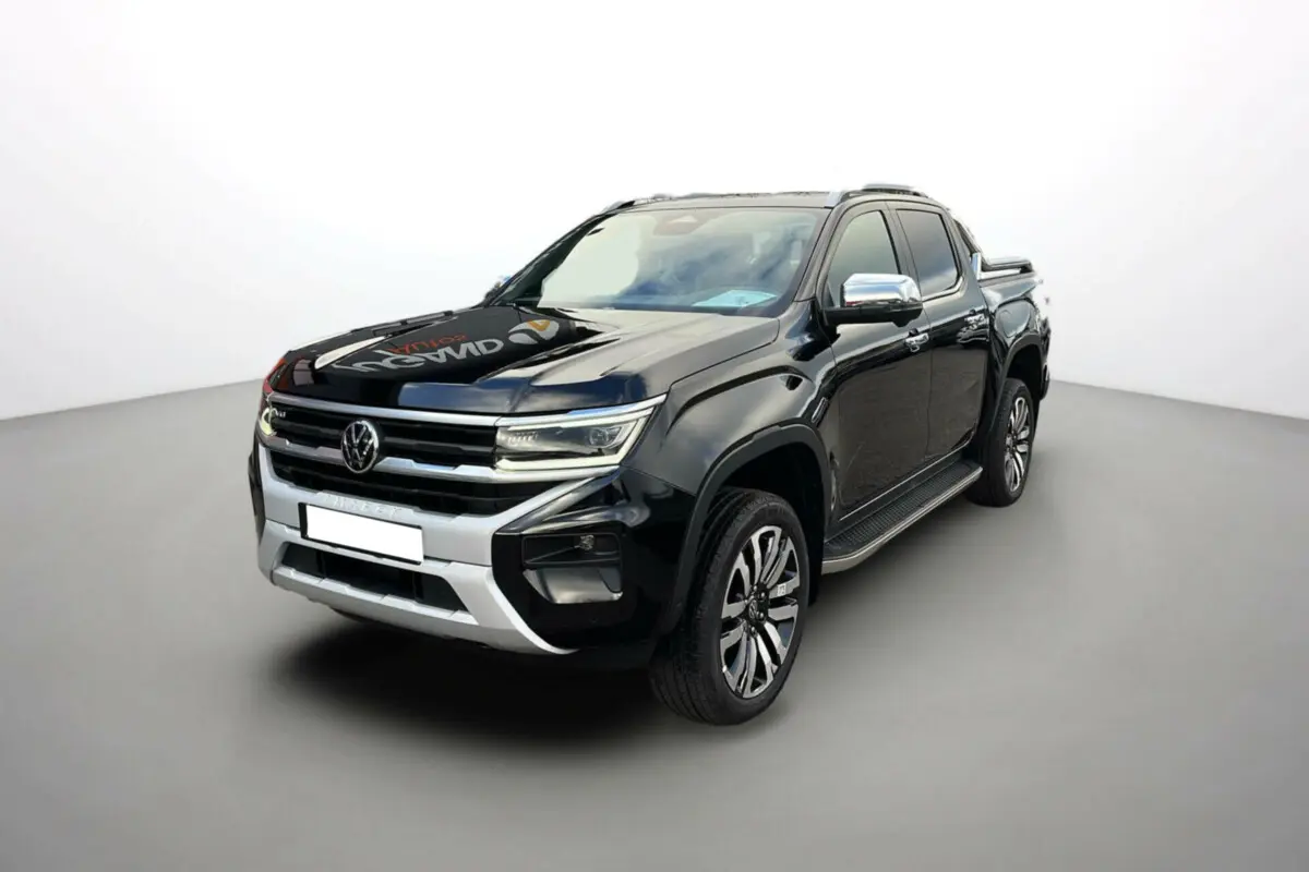Volkswagen Amarok V6 noir en 3/4 avant droit avec jantes alu 21 pouces et barres de toit visibles.