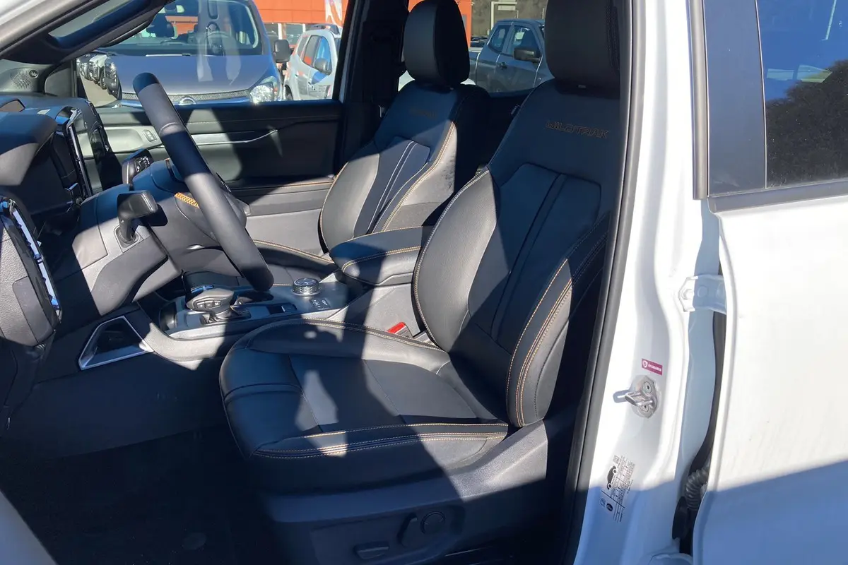 Vue intérieure côté conducteur du Ford Ranger Wildtrak blanc glacier, sièges cuir noirs avec surpiqûres orange et logo Wildtrak brodé.
