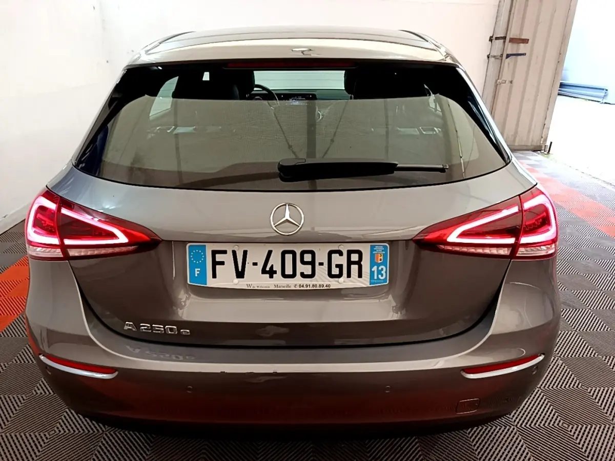 Vue arrière d'une Mercedes Classe A 250 e hybride rechargeable gris métallisé avec feux LED allumés dans un garage.