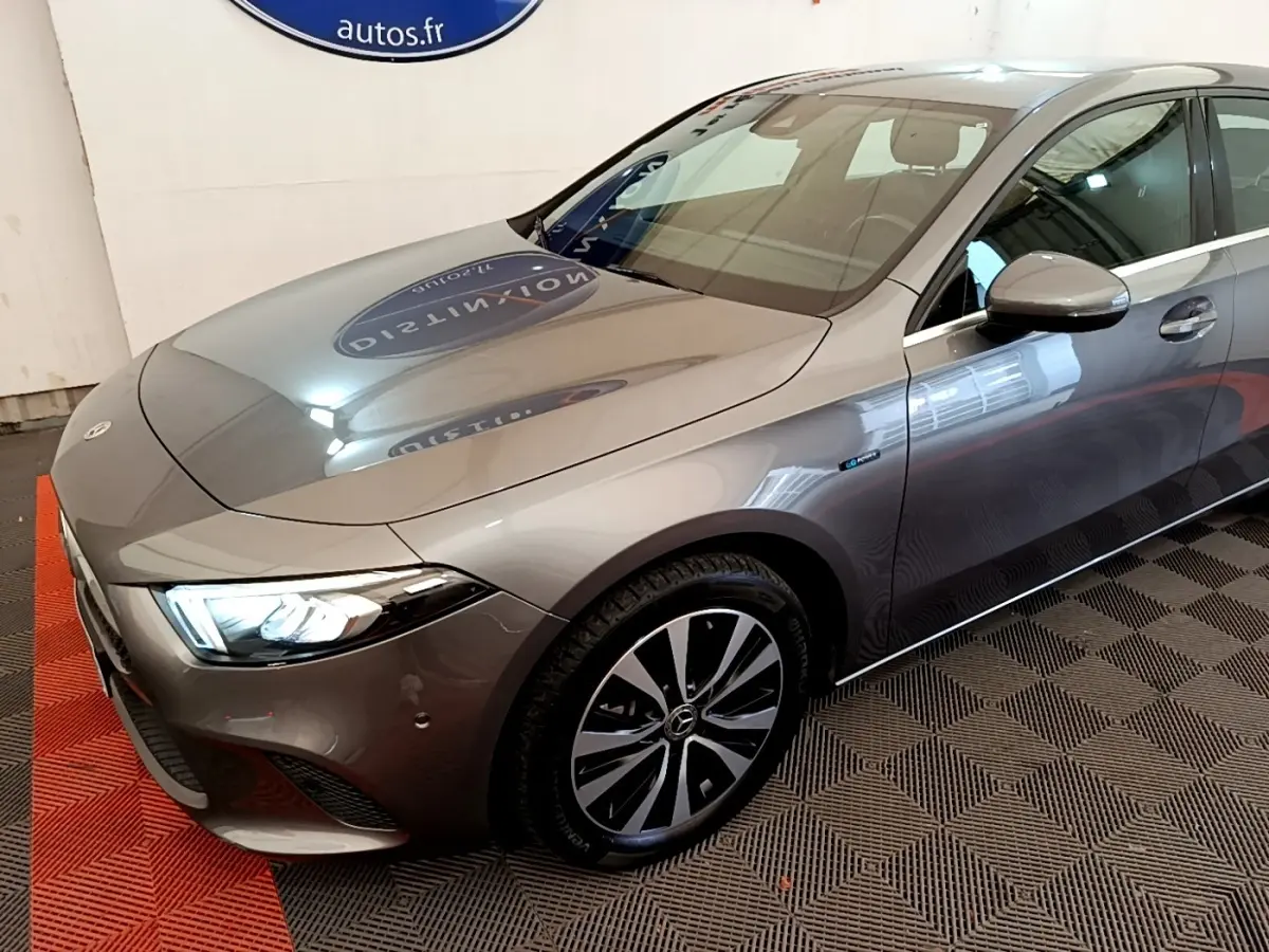 Mercedes Classe A 250 e Business Line gris métallisé vue 3/4 avant droit avec phares LED allumés et jantes distinctives.