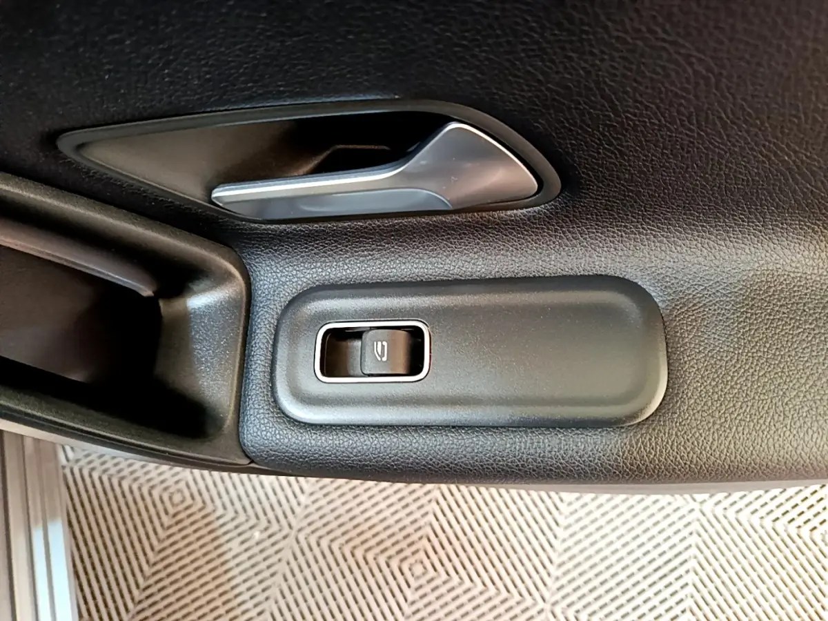 Détail de la poignée intérieure et bouton de lève-vitre électrique côté gauche d'une Mercedes Classe A hybride rechargeable noire.