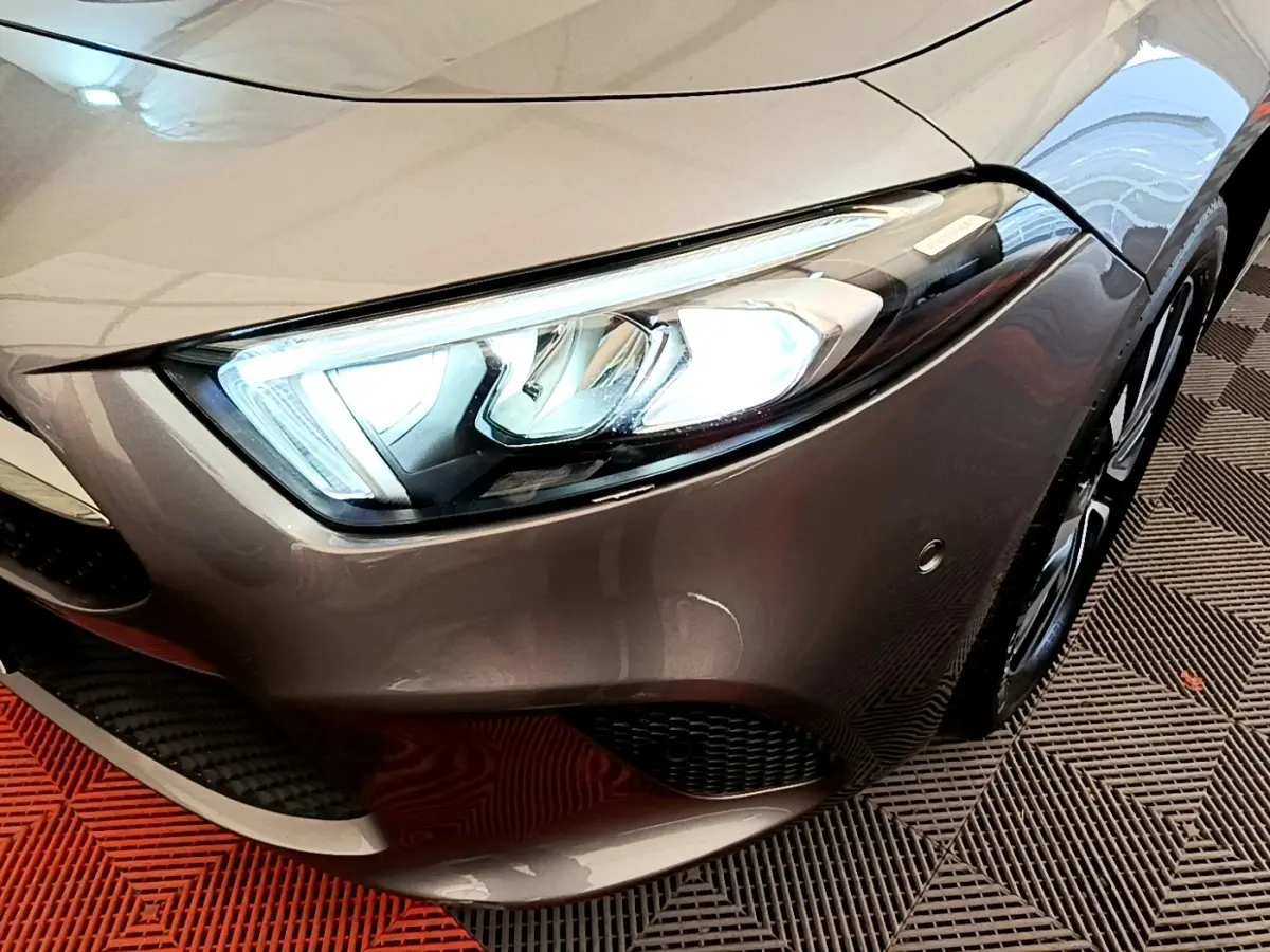 Gros plan sur le phare avant droit d’une Mercedes Classe A 250 e Business Line gris métallisé avec jante alliage visible.