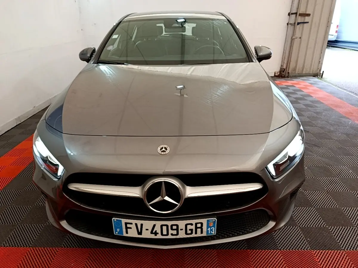 Vue avant d'une Mercedes Classe A grise avec phares allumés, calandre chromée et logo central visible.