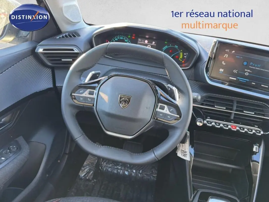 Vue intérieure centrée sur le volant cuir et le tableau de bord numérique de la Peugeot 208 gris 2025.