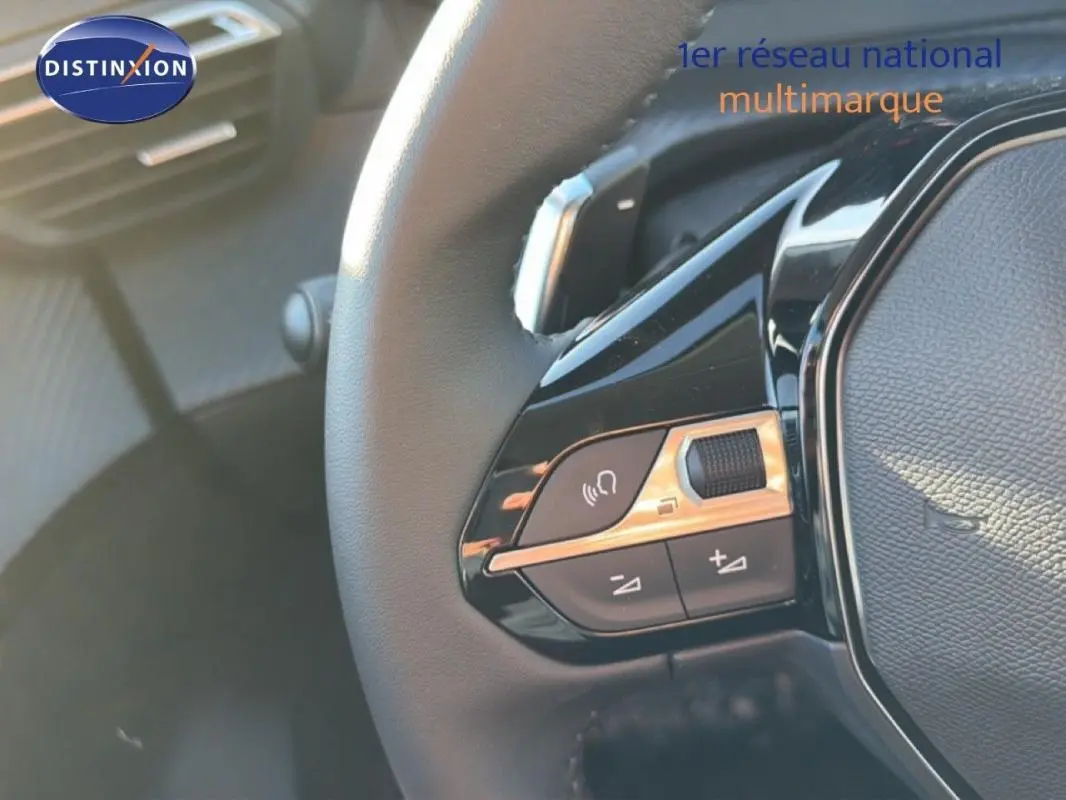 Gros plan sur le volant cuir de la Peugeot 208 gris, avec commandes intégrées et palettes au volant visibles.