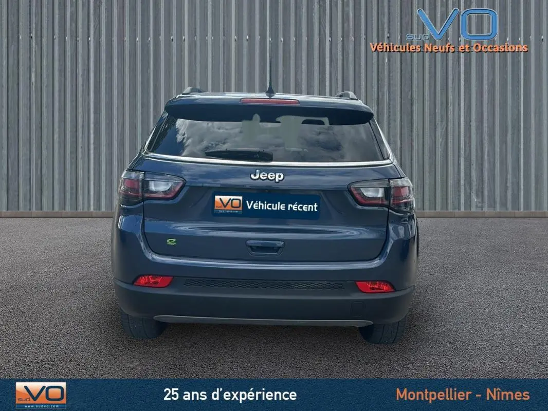 Vue arrière d'un Jeep Compass bleu 2023 avec feux LED et barres de toit visibles sur fond urbain.